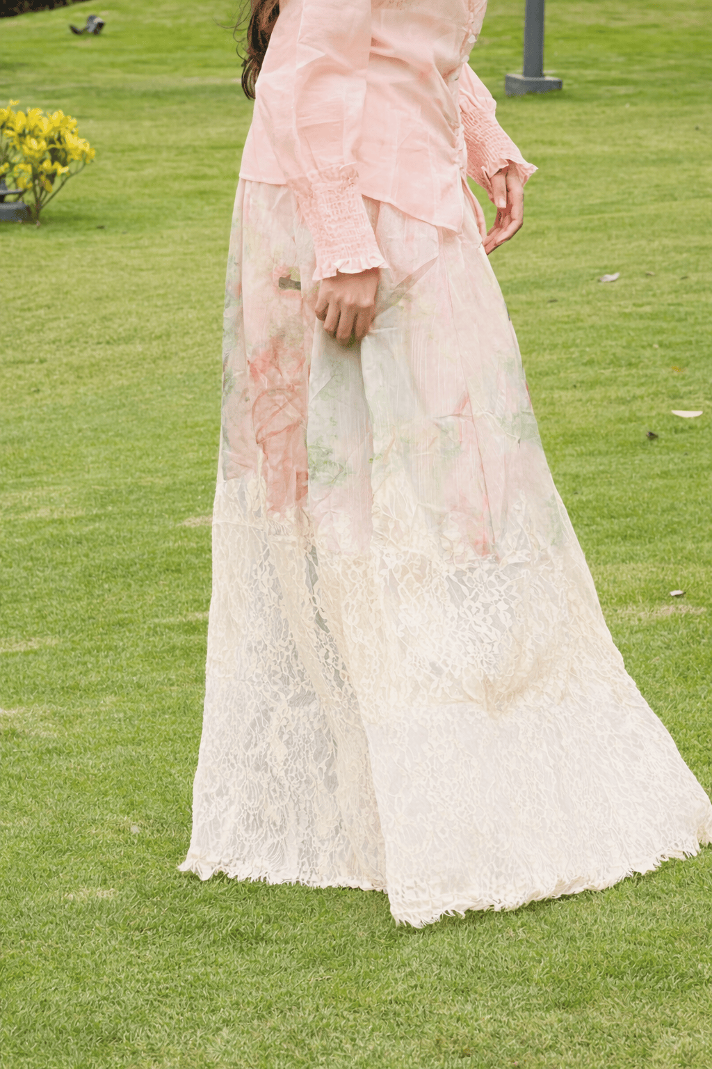 Person wearing a light pink floral blouse and white lace skirt on a grassy background