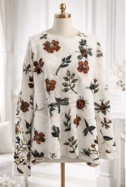 Floral and insect patterned sweater on a mannequin against a white background