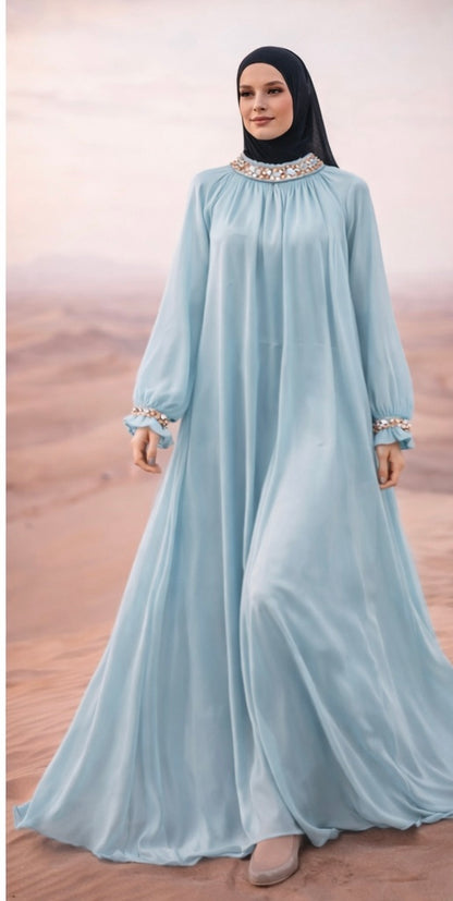 Woman wearing a light blue dress with long sleeves and a black hijab on a desert background