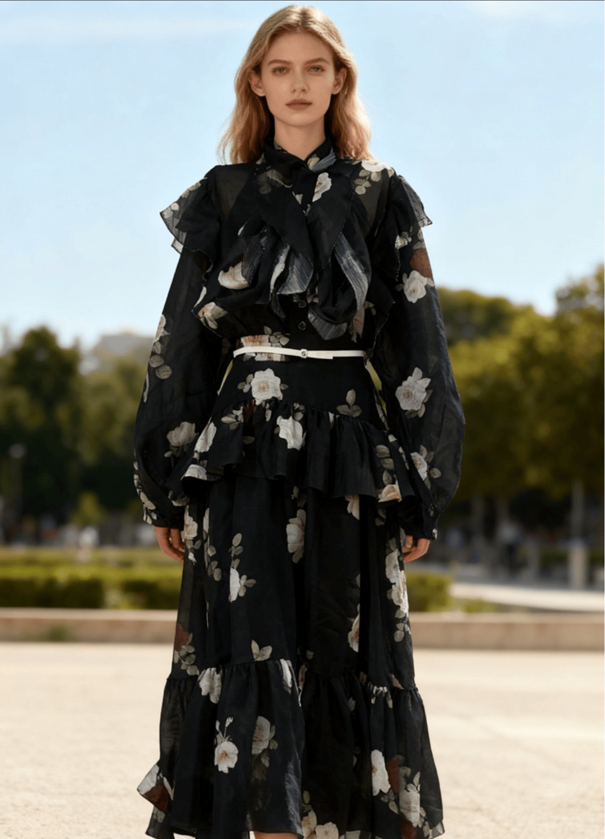 Woman wearing a black floral dress standing outdoors with trees and sky in the background