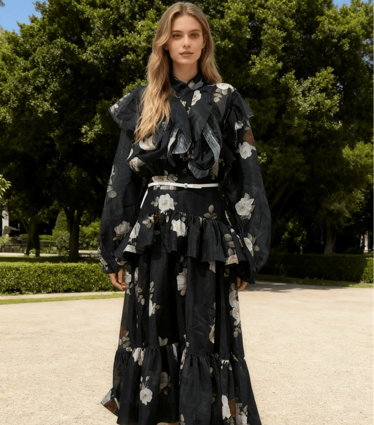 Woman in a black floral dress standing outdoors with trees in the background
