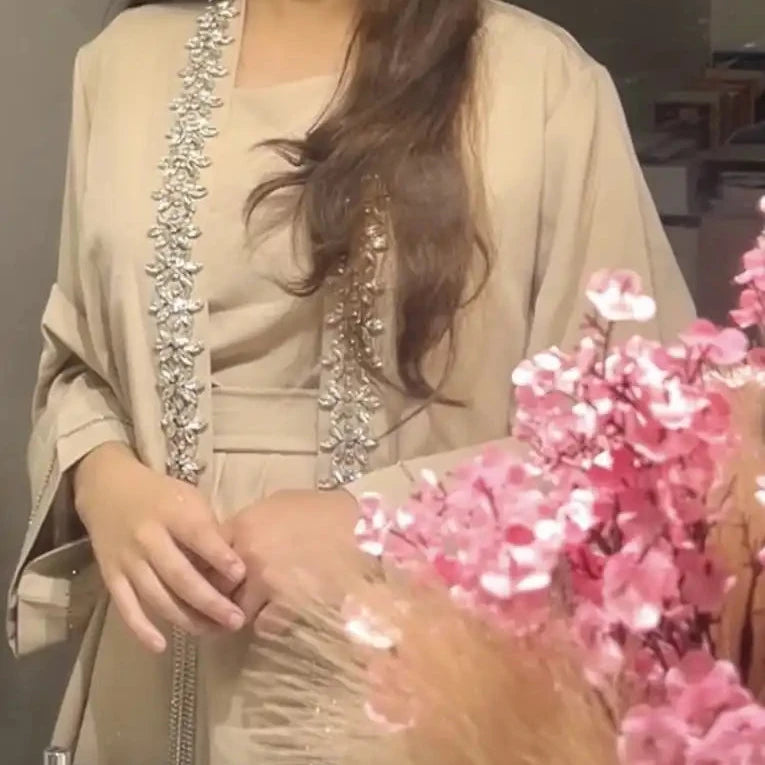 Woman in a beige traditional outfit with floral decorations in a room.