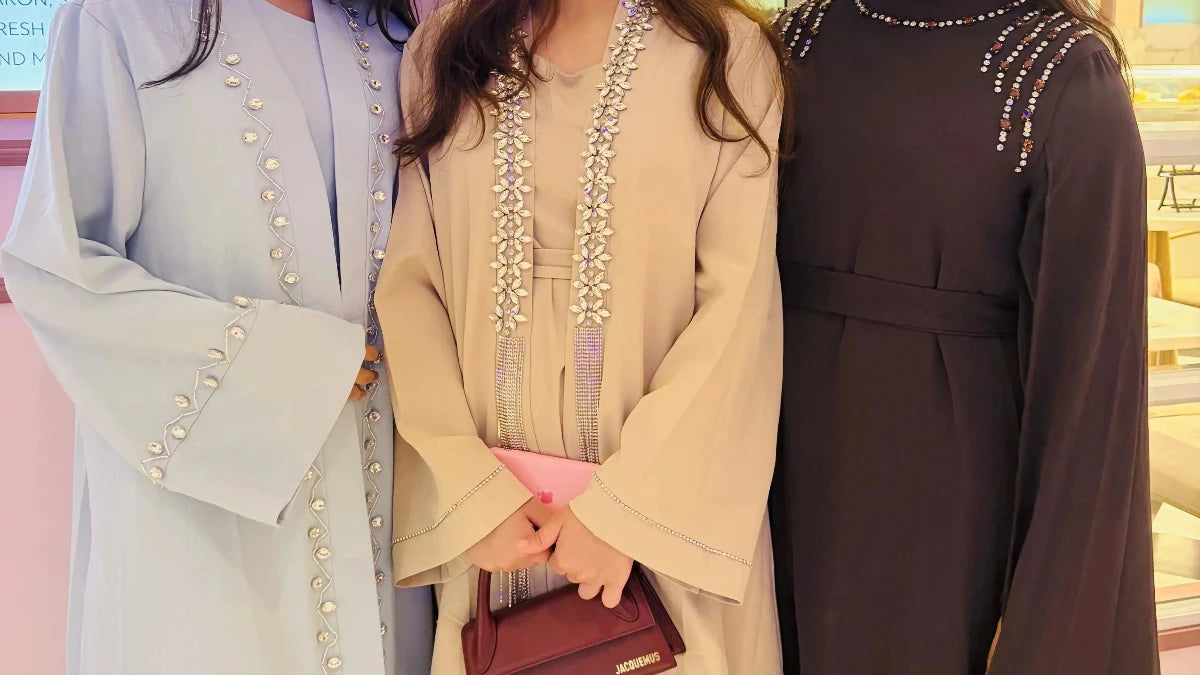 Three women in traditional outfits standing together, with one holding a red handbag.