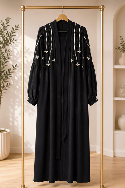 Black dress with pearl embellishments on a gold rack in a room with plants and shelves.