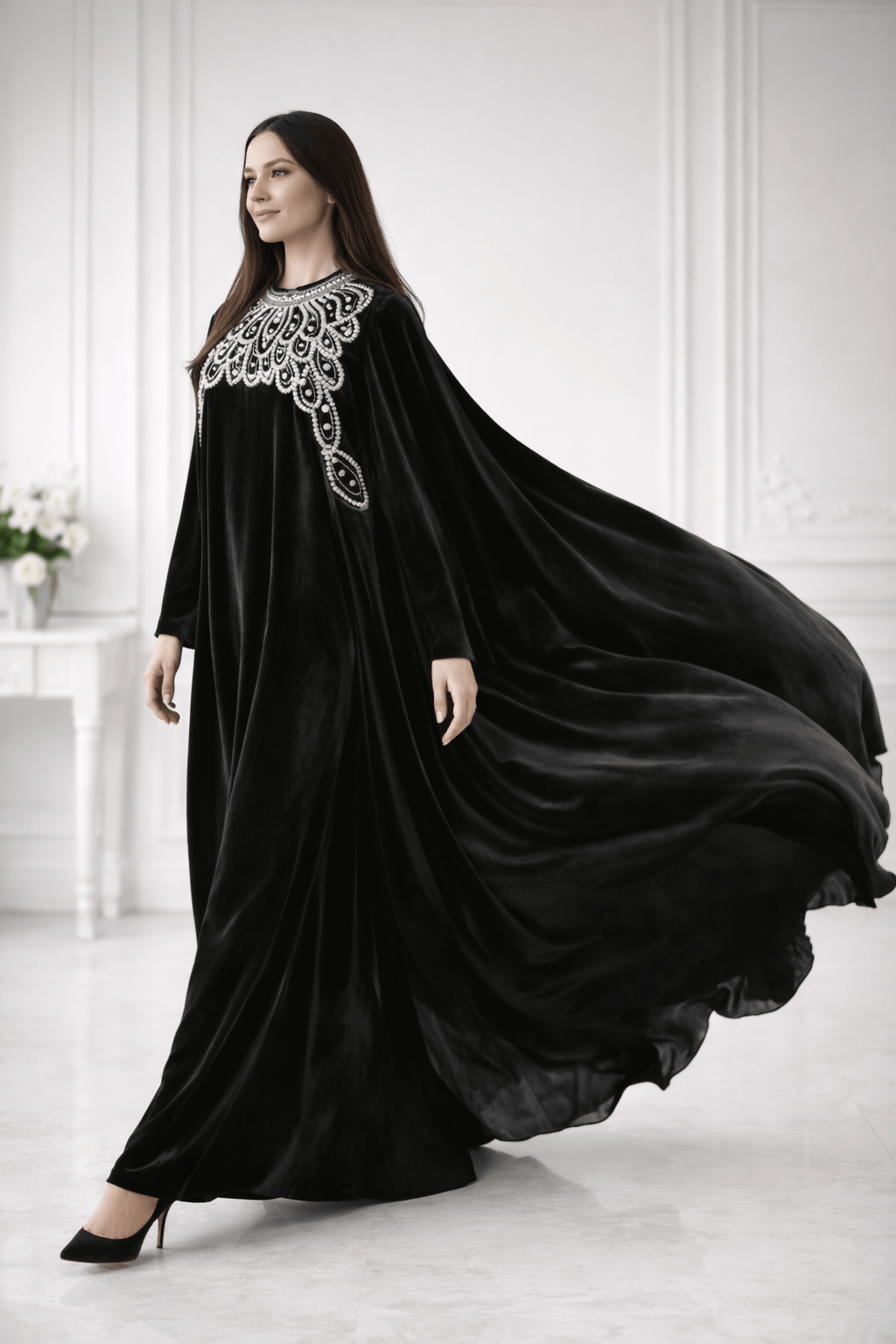 Woman wearing a black abaya with white embroidery in a white room.