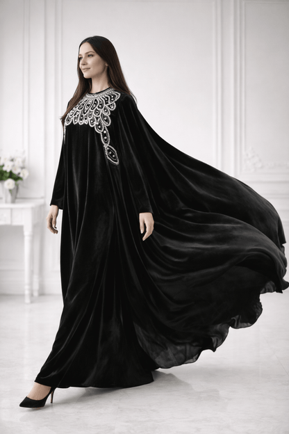Woman wearing a black abaya with white embroidery in a white room.
