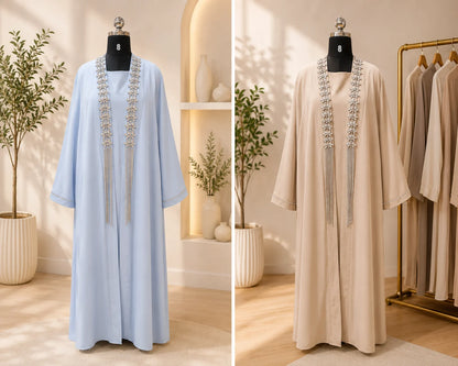 Two abayas, one light blue and one beige, on mannequins with decorative elements in a well-lit room.