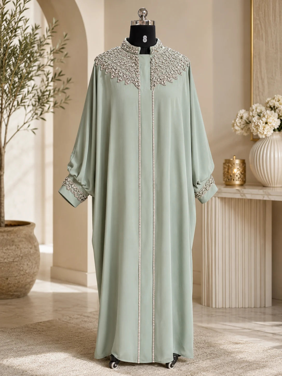 Light green abaya with intricate detailing on a mannequin against a neutral background.