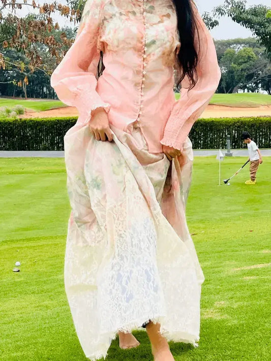 Woman in a floral dress standing on a golf course with a child playing in the background.